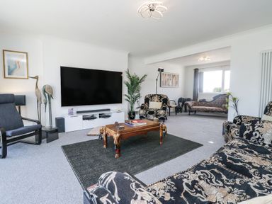 A living room with a large television on a white stand a wooden coffee table patterned sofas and armchairs and a large window at Eildon Lodge in Gosforth