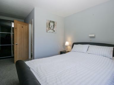 A bedroom with a bed striped bedding a bedside table with a lamp an open wooden door and a painting on the wall at Eildon Lodge in Gosforth