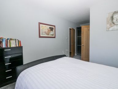A bedroom with a bed, a black dresser with books, wall art, and two doors at Eildon Lodge in Gosforth
