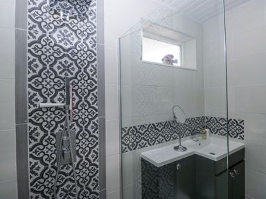A bathroom with patterned tiles a shower head a sink with a mirror and toiletries at Eildon Lodge in Gosforth