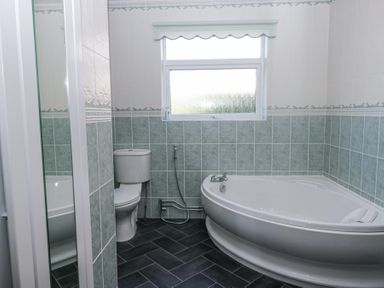A bathroom with a corner bathtub a toilet a window and green and white tiled walls at Eildon Lodge in Gosforth