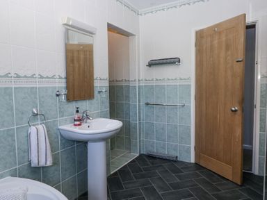 A bathroom with a pedestal sink a mirror a towel rail and an open wooden door at Eildon Lodge in Gosforth
