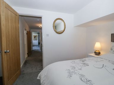 A bedroom with a bed a bedside lamp a wall mirror and an open door leading to a hallway at Eildon Lodge in Gosforth