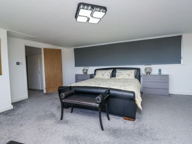 A bedroom with a bed a bench two bedside tables and grey carpet at Eildon Lodge in Gosforth