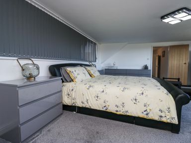 A bedroom with a large bed with floral bedding and gray furniture at Eildon Lodge in Gosforth