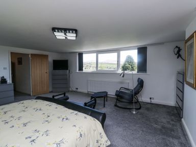 A bedroom with a bed a rocking chair and large window at Eildon Lodge in Gosforth