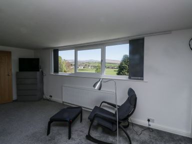 A room with a rocking chair and footstool near a window with a view of fields and hills at Eildon Lodge in Gosforth