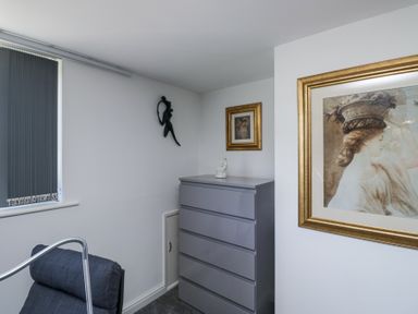 A corner of a room with a gray chest of drawers a black chair a small white statue and framed artwork on white walls at Eildon Lodge in Gosforth