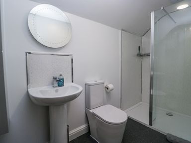 A bathroom with a pedestal sink, round mirror, toilet, and a glass shower enclosure at Eildon Lodge in Gosforth