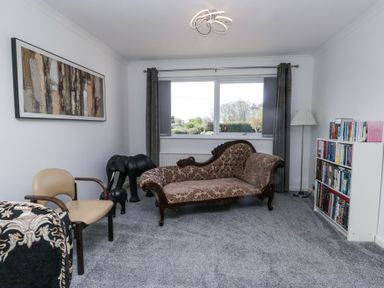 A sitting room with a patterned chaise lounge a beige chair two elephant statues a bookshelf and a floor lamp at Eildon Lodge in Gosforth
