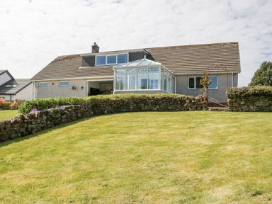 A house with a glass conservatory and a stone wall in a garden at Eildon Lodge in Gosforth