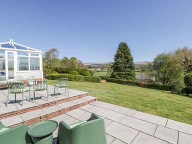 A patio with green chairs and tables overlooking a lawn and trees at Eildon Lodge in Gosforth