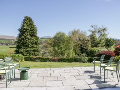 An outdoor patio with chairs and a small table overlooking a garden with trees and hills at Eildon Lodge in Gosforth