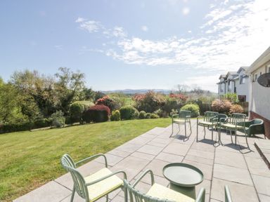A garden patio with multiple chairs and a small table overlooking a lawn and bushes at Eildon Lodge in Gosforth