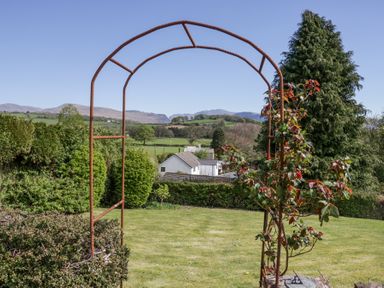 A garden with a metal arch and plants with houses and hills in the background at Eildon Lodge in Gosforth