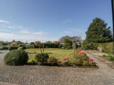A garden with trimmed bushes gravel path and lawn under a blue sky at Eildon Lodge in Gosforth