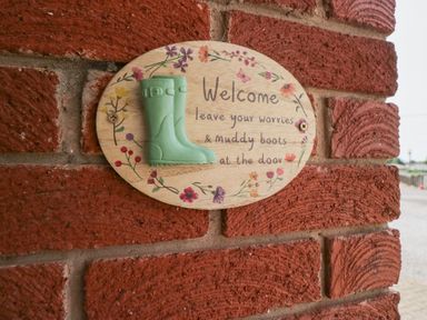 A welcome sign with a green boot and flowers on a brick wall at Eildon Lodge in Gosforth