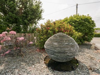 An outdoor garden with a stone sculpture surrounded by plants and gravel at Eildon Lodge in Gosforth