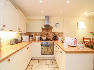 A kitchen with white cabinets wooden countertops and tiled backsplash at Fox Hat Cottage in Chagford