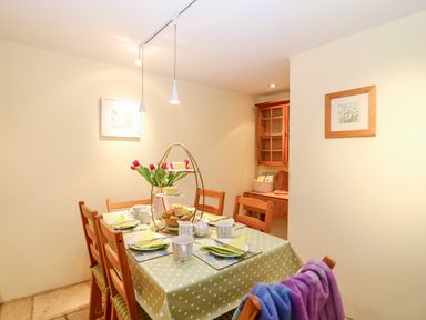 A dining area with a table covered in a green polka dot tablecloth set with cups plates and napkins and wooden chairs at Fox Hat Cottage in Chagford