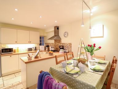A kitchen with wooden cabinets and a dining table set with cups and plates at Fox Hat Cottage in Chagford