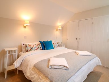 A bedroom with a bed with pillows and folded towels with wall lights and wardrobes at Fox Hat Cottage in Chagford