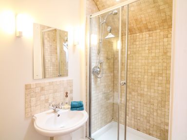 A bathroom with a shower enclosure and a sink with a mirror and towel at Fox Hat Cottage in Chagford