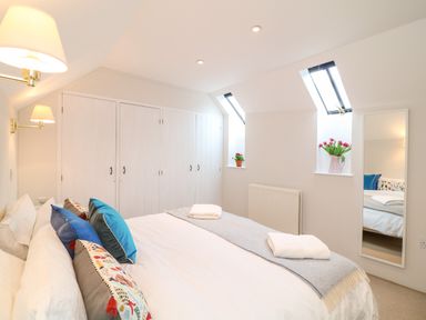 A bedroom with a bed with pillows and folded towels next to built in wardrobes and two skylights with flowers at Fox Hat Cottage in Chagford