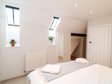 A bedroom with a bed folded towels on top two windows with flower pots and a white door at Fox Hat Cottage in Chagford
