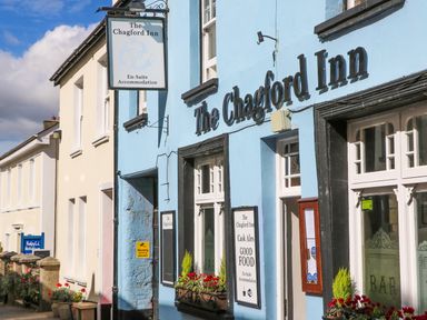 Exterior view of The Chagford Inn with blue facade windows flower boxes and signs in Chagford