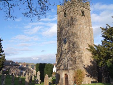 A stone church tower with clock surrounded by gravestones and trees at Fox Hat Cottage in Chagford