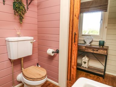 A bathroom with a toilet with wooden seat and pink walls next to a wooden console table under a window at Westfield Lodge in Terrington near Sheriff Hutton