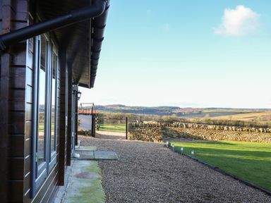 Exterior view of a wooden building with glass windows a gravel pathway a stone wall and fields at Westfield Lodge in Terrington near Sheriff Hutton