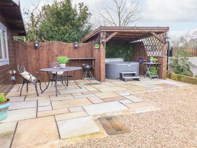 A patio area with a metal table and two chairs a barbecue grill and a covered hot tub at Westfield Lodge in Terrington near Sheriff Hutton