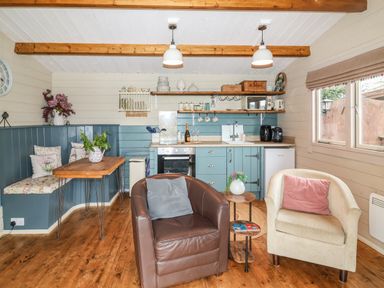 A kitchen with blue cabinets a wooden table with bench seating two armchairs and shelves with kitchen items at Westfield Lodge in Terrington near Sheriff Hutton