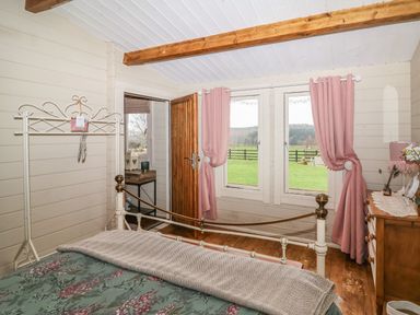 A bedroom with a metal bed floral bedding pink curtains wooden dresser and a doorway at Westfield Lodge in Terrington near Sheriff Hutton