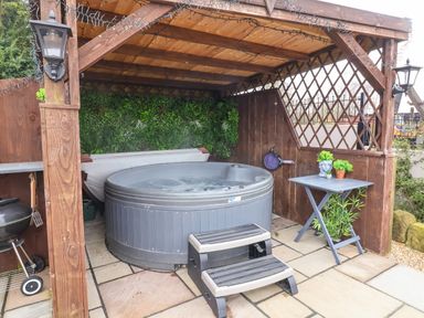 An outdoor hot tub with steps under a wooden gazebo next to a small table with plants at Westfield Lodge in Terrington near Sheriff Hutton