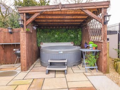 An outdoor wooden gazebo with a hot tub table with plants and a barbecue on a paved patio at Westfield Lodge in Terrington near Sheriff Hutton
