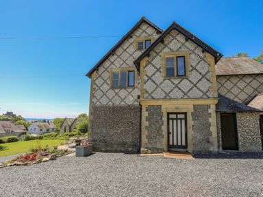 An exterior view of a two-story house with pebble dash walls and a gravel driveway at Bryn Henllan in Criccieth
