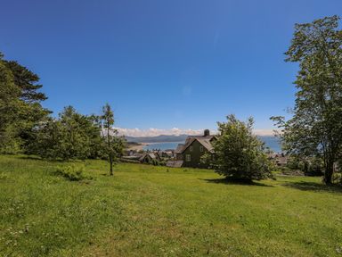 A grassy field with trees and houses with a distant view of the sea and mountains at Bryn Henllan in Criccieth