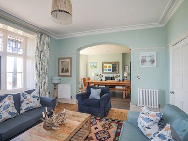 A living room with blue sofas and a wooden coffee table next to a dining area at Bryn Henllan in Criccieth