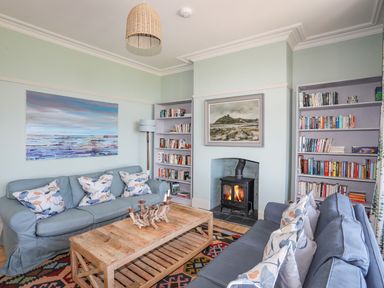 A living room with two blue sofas, a wooden coffee table, bookshelves, a fireplace with a painting above it, and a floor lamp at Bryn Henllan in Criccieth