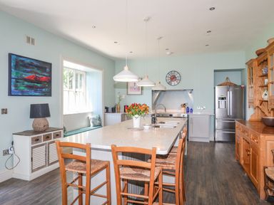 A kitchen with a large island and wooden chairs next to stainless steel refrigerator and wooden cupboard at Bryn Henllan in Criccieth
