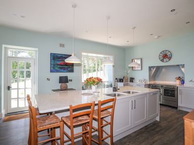 A kitchen with an island counter with stools pendant lights oven and a door at Bryn Henllan in Criccieth