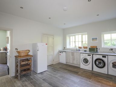 A utility room with a refrigerator washing machines dishwasher and wooden crate storage at Bryn Henllan in Criccieth