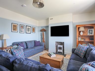 A living room with two blue sofas a wooden coffee table a bookshelf and a wall mounted television at Bryn Henllan in Criccieth