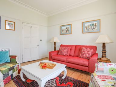 A living room with a red sofa two lamps a white coffee table and colorful armchairs at Bryn Henllan in Criccieth