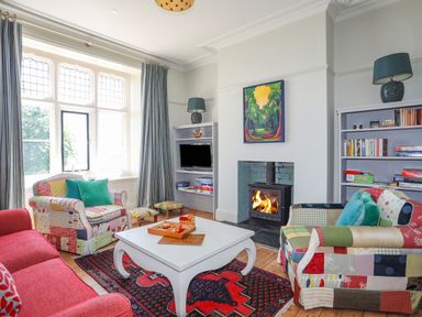 A living room with colorful patchwork armchairs a red sofa a white coffee table and a wood burning stove at Bryn Henllan in Criccieth