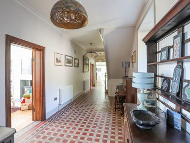A hallway with patterned tile floor paintings on walls and wooden furniture at Bryn Henllan in Criccieth