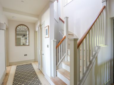 A hallway with wooden stairs and a patterned black and white rug at Bryn Henllan in Criccieth